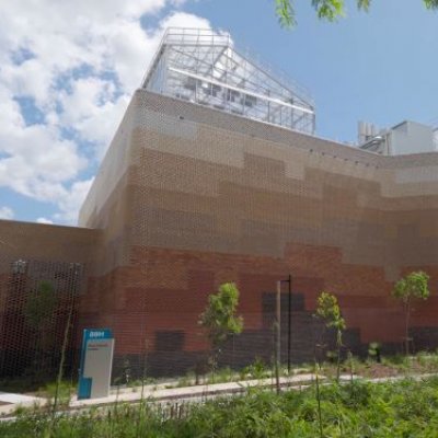 a large brick building against a blue sky with glasshouses on its roof